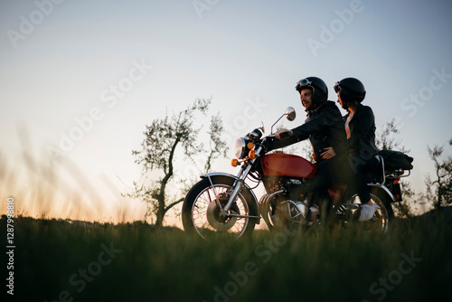 Young couple on vintage motorbike in rural scene at sunset photo