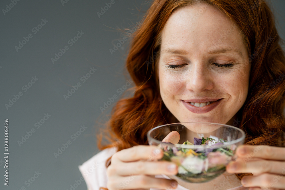 Portrait of smiling redheaded woman smelling blossoms in glass bowl Portrait of smiling redheaded woman smelling blossoms in glass bowl