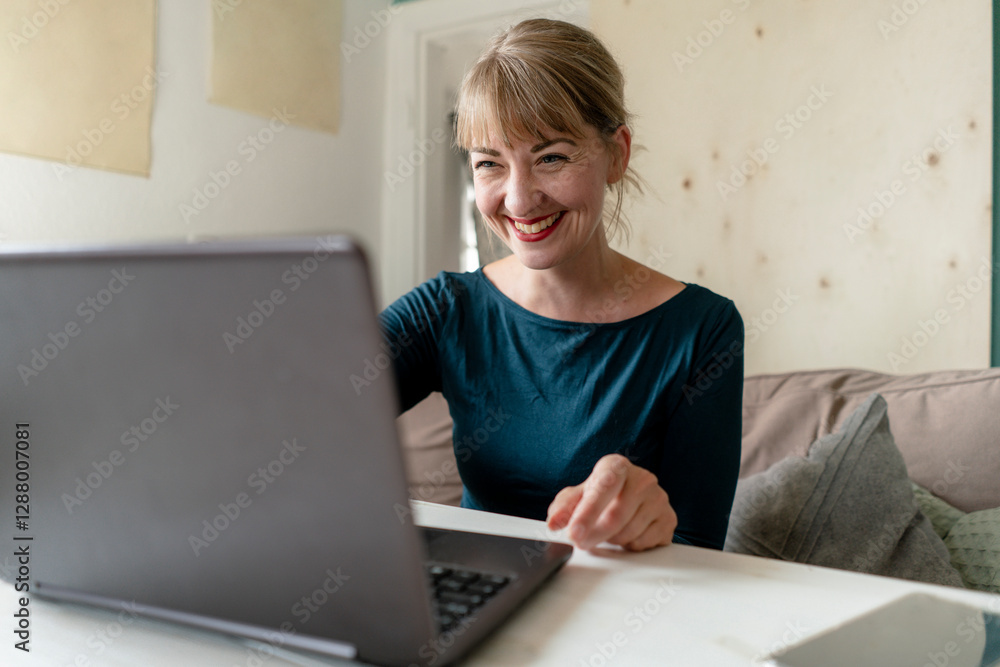 Portrait of laughing woman sitting at table at home using laptop Portrait of laughing woman sitting at table at home using laptop