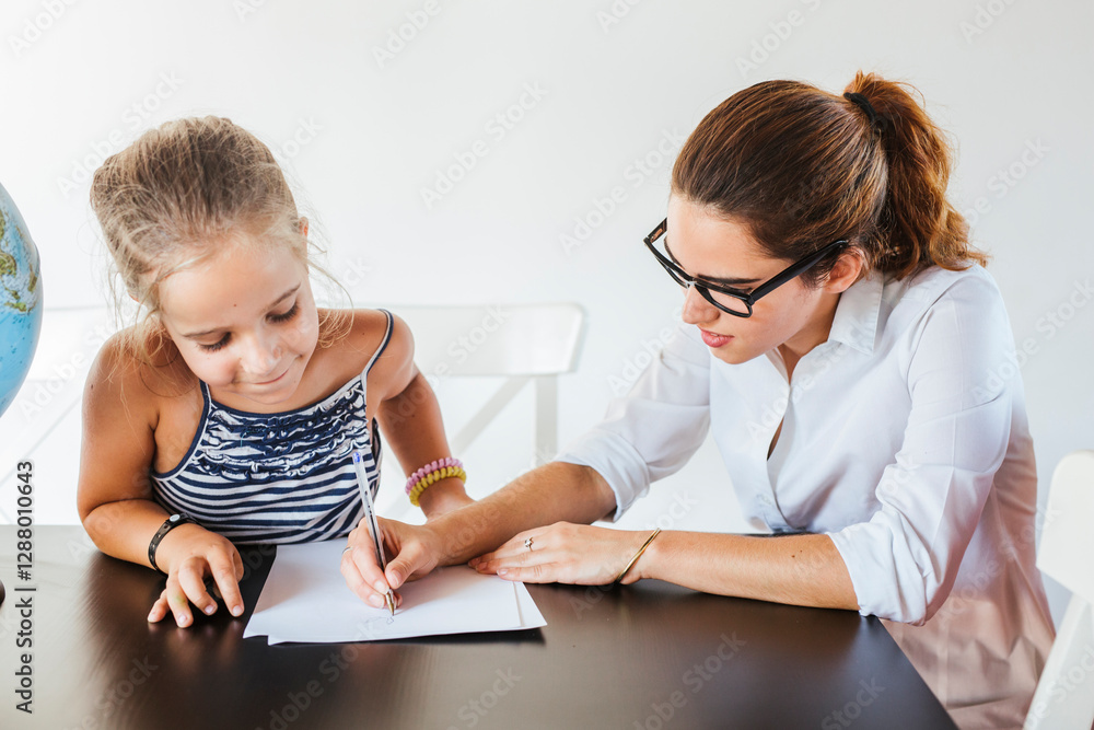 Teacher helping schoolgirl at desk writing on paper Teacher helping schoolgirl at desk writing on paper