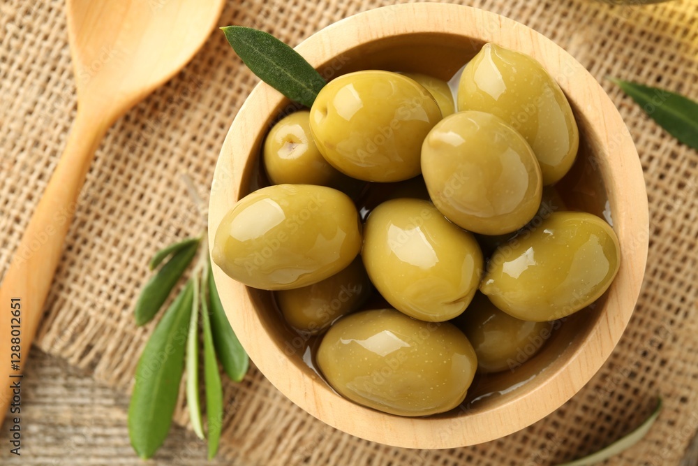 Delicious marinated olives in bowl, green leaves and spoon on table, flat lay Delicious marinated olives in bowl, green leaves and spoon on table, flat lay