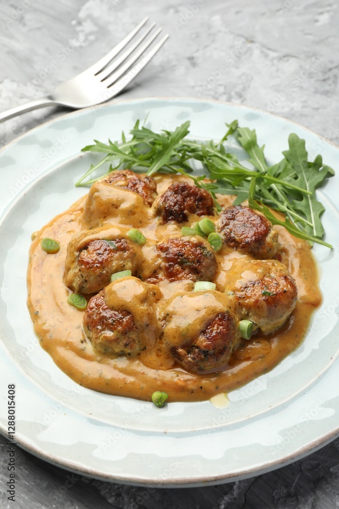 Delicious meatballs with gravy cream sauce, herbs and arugula served on grey table, closeup Delicious meatballs with gravy cream sauce, herbs and arugula served on grey table, closeup