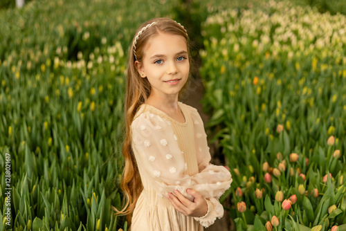 A cute charming girl in a light dress is photographed in a greenhouse with tulip flowers. Women's Day photo