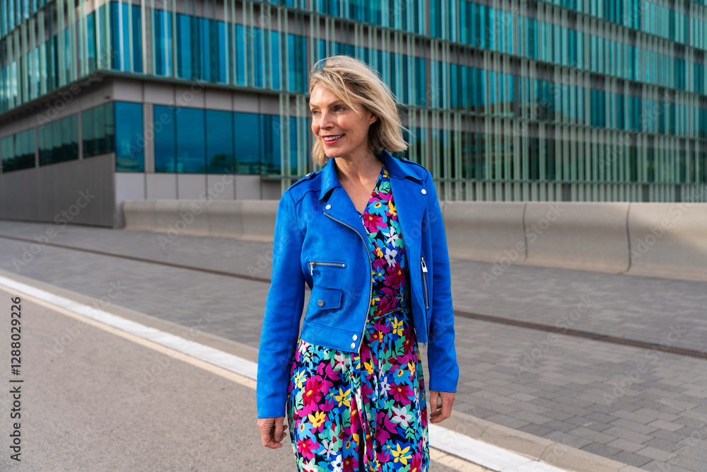 Woman in colorful dress and blue jacket strolling in urban setting Woman in colorful dress and blue jacket strolling in urban setting