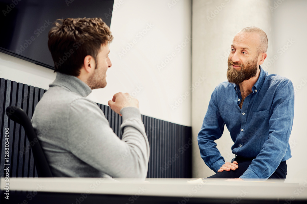 Two colleagues in a casual meeting discussing business in an office setting Two colleagues in a casual meeting discussing business in an office setting