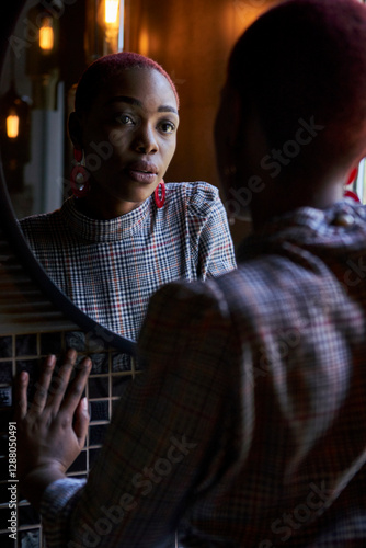 Black woman with short fun haircut looking to her reflection in a round mirror photo