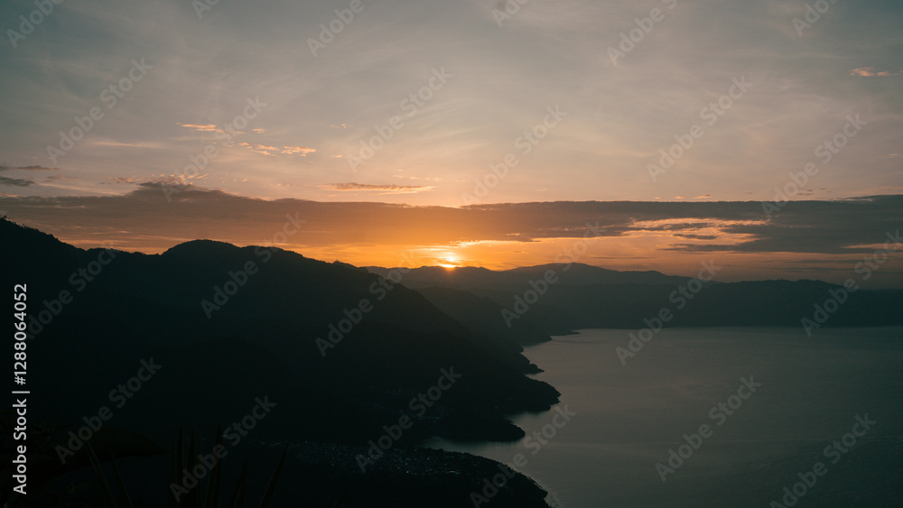 Obraz premium The sun rising behind majestic mountains, casting a warm glow over the tranquil lake