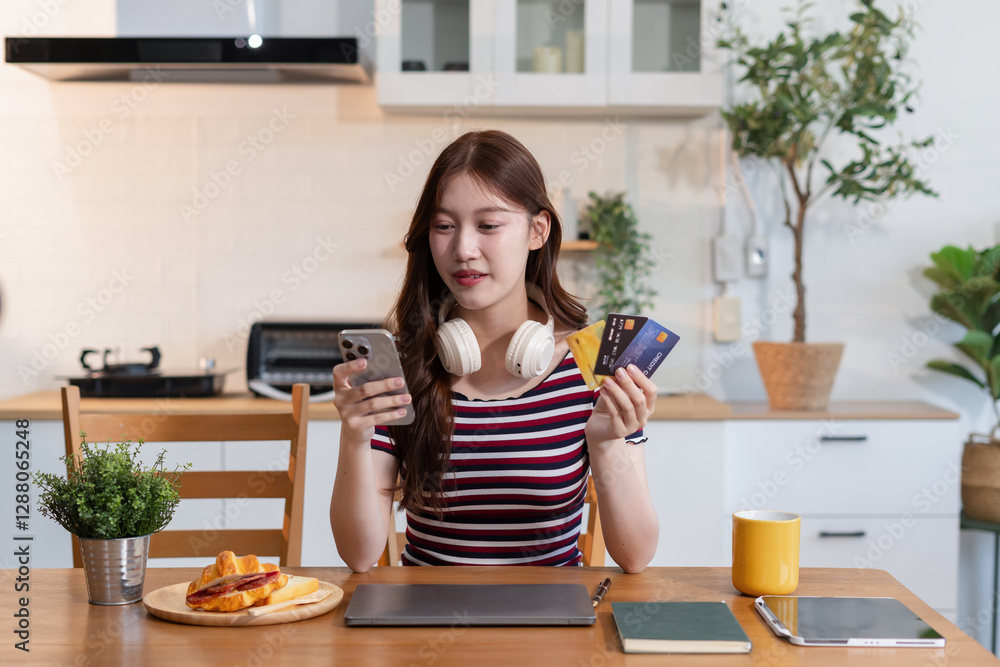 Happy smiling women hold credit cards, conduct financial transactions via smartphone sitting in the kitchen. Happy smiling women hold credit cards, conduct financial transactions via smartphone sitting in the kitchen.