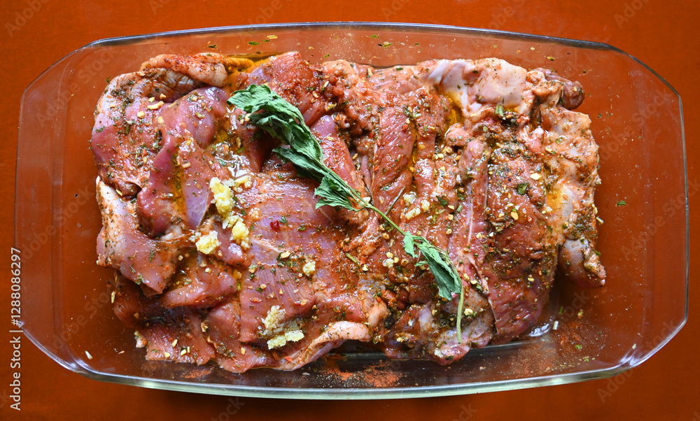 Marinated meat with herbs and spices in a glass dish ready for cooking at a kitchen counter