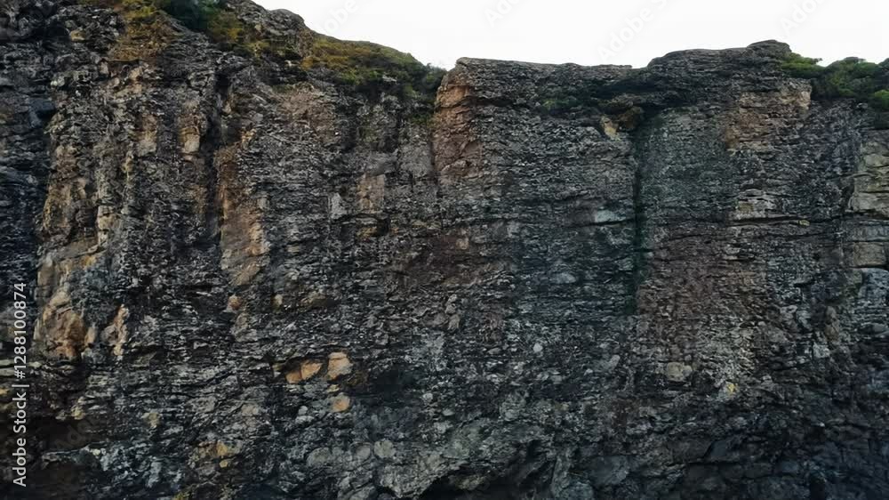 Slow pan across a rocky cliff face with patches of dark and light stone under gentle lighting Slow pan across a rocky cliff face with patches of dark and light stone under gentle lighting