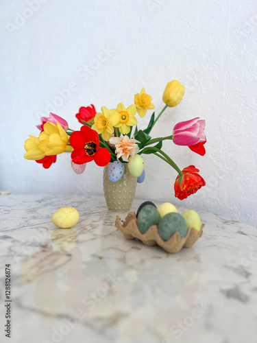 An Easter card. Colorful bright tulips decorated with eggs are in a vase on the table next to colorful eggs. Vertical photography