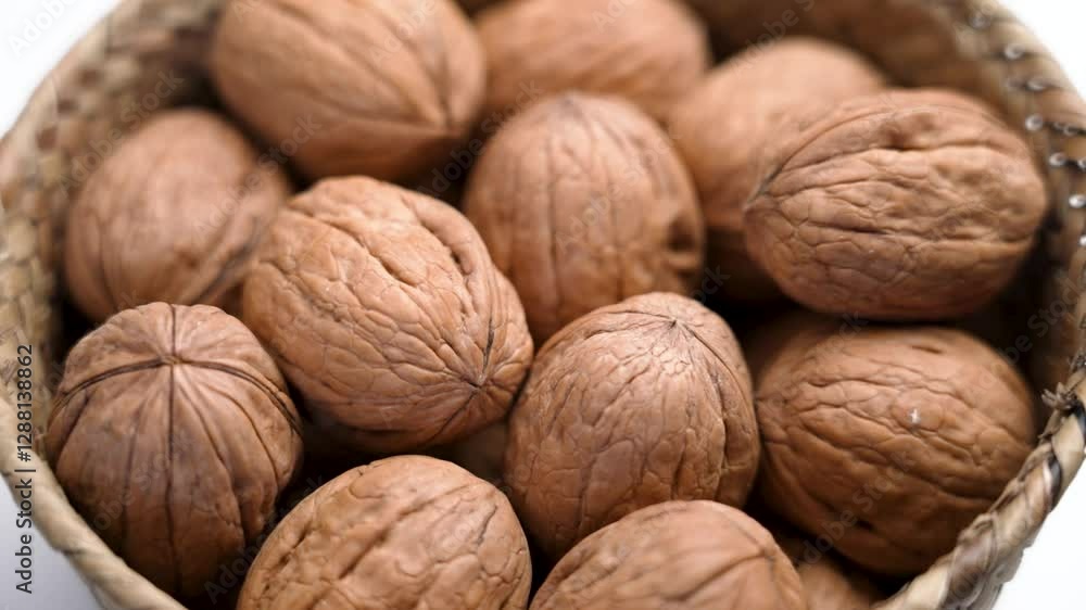 Whole unshelled organic walnut falling into a rustic wicker bowl in slow motion on white table. Protein nutritious nut snack Whole unshelled organic walnut falling into a rustic wicker bowl in slow motion on white table. Protein nutritious nut snack