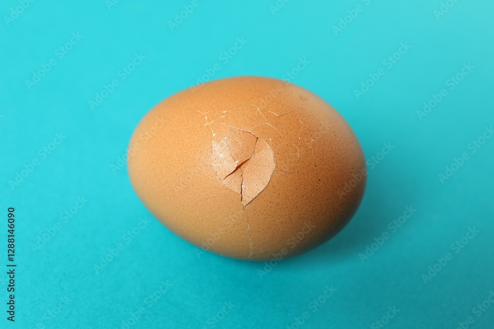 One egg with cracked shell on light blue background, closeup One egg with cracked shell on light blue background, closeup