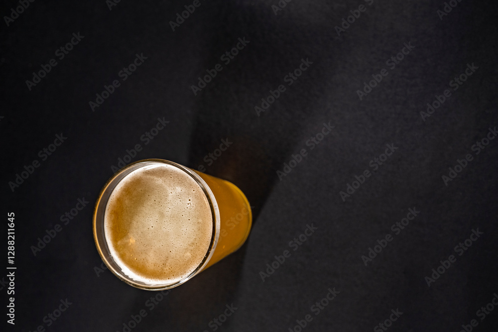 tall glass of golden beer with a frothy head sits slightly off-center on a black chalkboard background, with empty space on the left