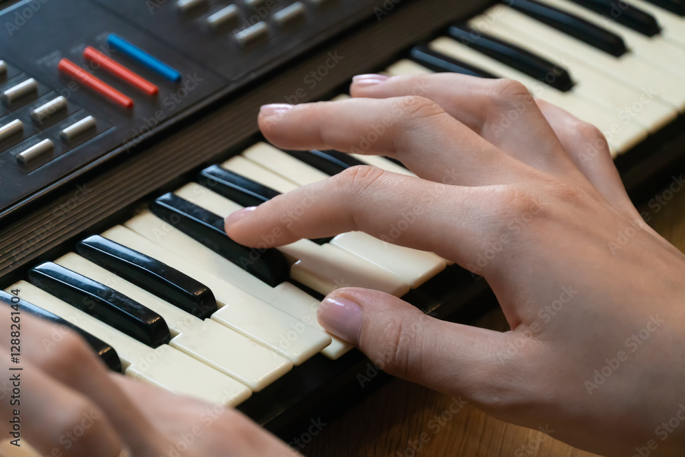Fototapeta premium Close-up of female hands playing a vintage synthesizer keyboard, creating electronic music in a home studio setting, showcasing musical creativity and passion