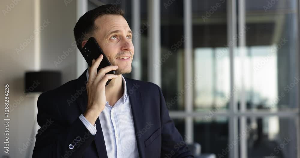Serious Hispanic business executive man in formal jacket talking on mobile phone in office hall space, speaking on cellphone, making call, smiling, looking away, enjoying communication Serious Hispanic business executive man in formal jacket talking on mobile phone in office hall space, speaking on cellphone, making call, smiling, looking away, enjoying communication