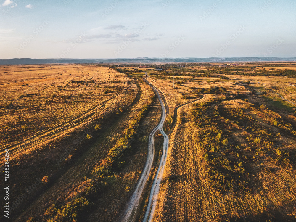 Naklejka premium Sunset Over a Village Road – Aerial Drone View of Open Fields and Countryside Landscape