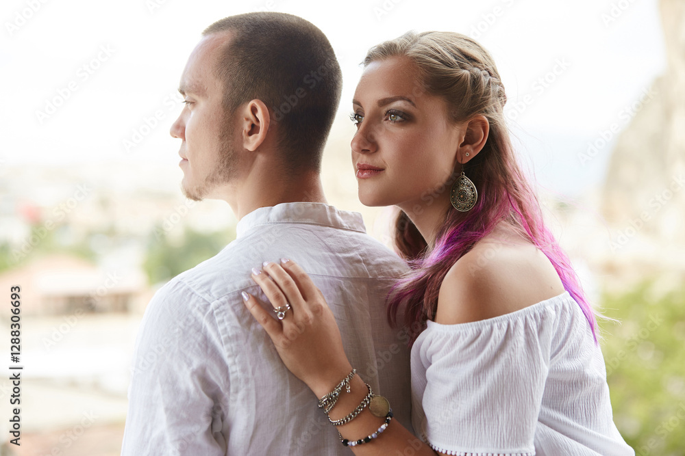 Obraz premium woman with colorful hair and a bright top leans gently against a man wearing a light shirt. They share a peaceful moment while admiring stunning scenery in the background