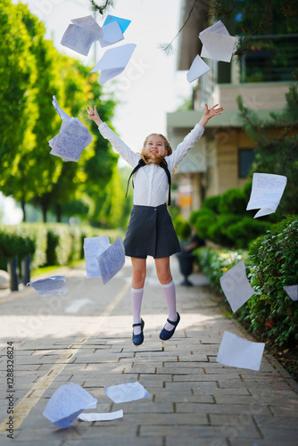 Happy cute schoolgirl dropping notebooks at the end of the school year.