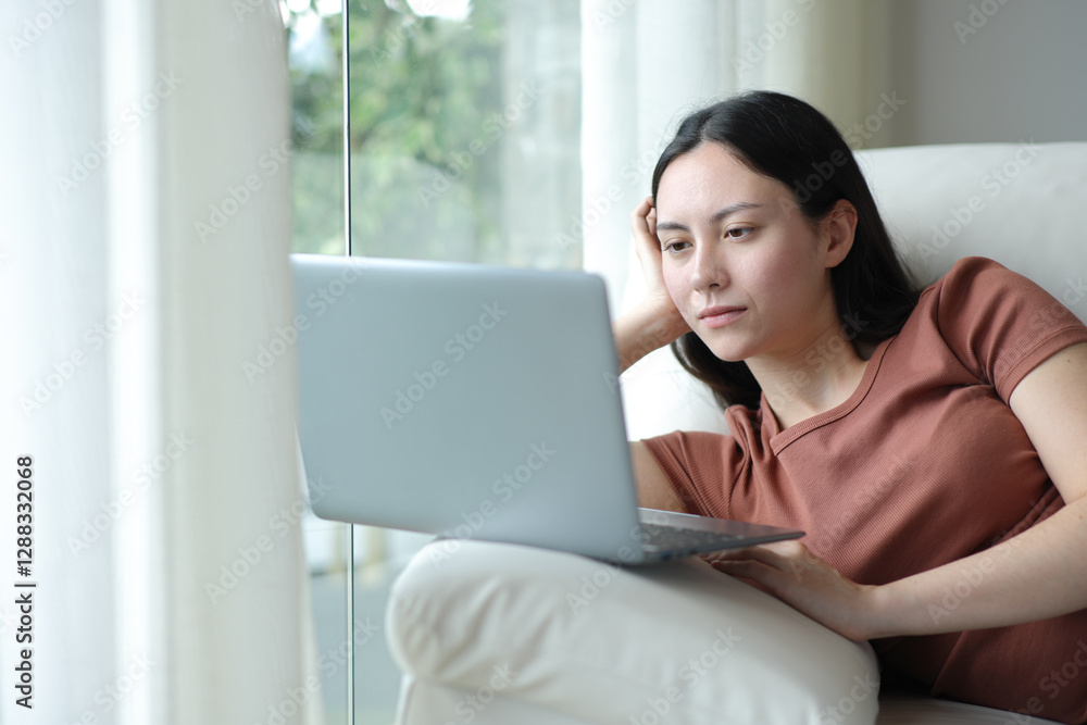 Fototapeta premium Serious asian woman using laptop relaxed on a couch