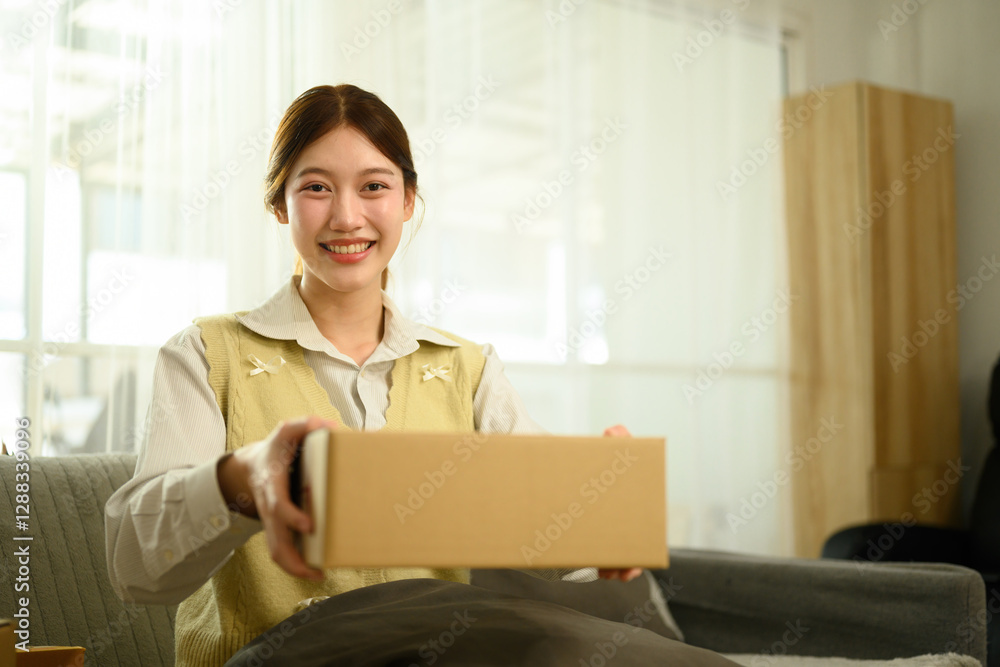 A cheerful young woman sits on a couch, happily presenting a delivery box, Your Order is Here