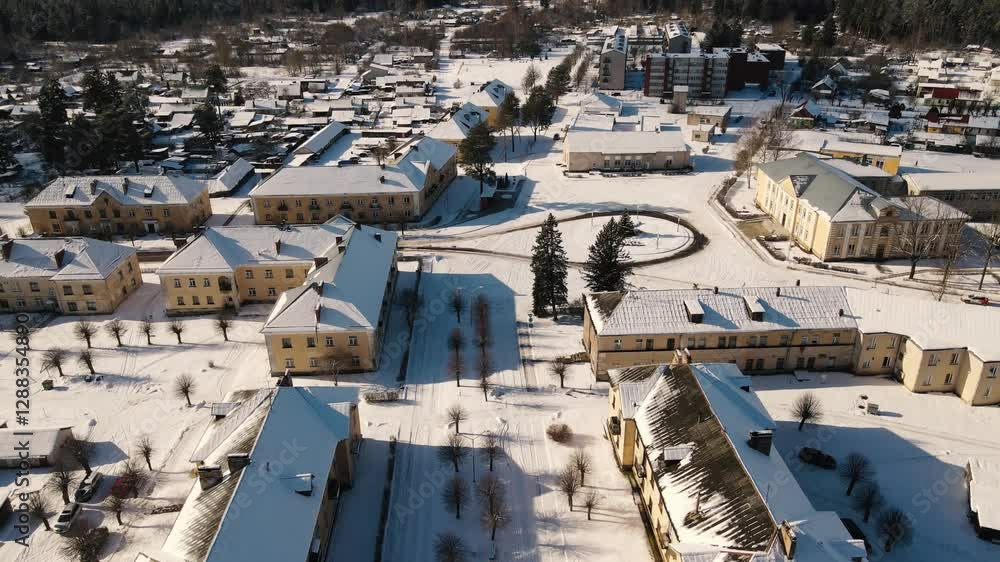 Aerial view of the snow-covered small town of Seda with yellow buildings, streets and roofs covered in white. A peaceful winter landscape in the sunlight. Aerial view of the snow-covered small town of Seda with yellow buildings, streets and roofs covered in white. A peaceful winter landscape in the sunlight.
