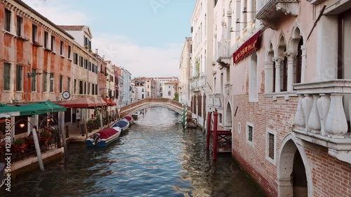 Venice, Italy - August 16 2024: Cozy corner Venice: narrow canal surrounded by pastel-colored buildings, gondolas with tourists bridge linking historic neighborhoods. Water mirrors warm shades walls.