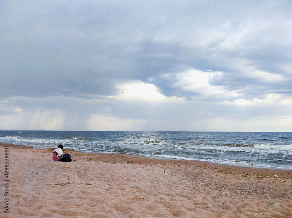 Obraz premium Woman sitting on sandy beach on seashore near sea with waves during rain. Dark storm clouds, rain and sea surface at sunset. Nature. Natural background. Stormy weather. Storm at sea.