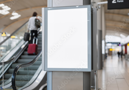 Empty billboard in airport terminal shows advertising potential with passenger using escalator in background