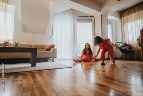 Photos Two cheerful young girls in colorful outfits enjoy playing on the hardwood floor of a sunlit living room, capturing the essence of fun and childhood friendship
