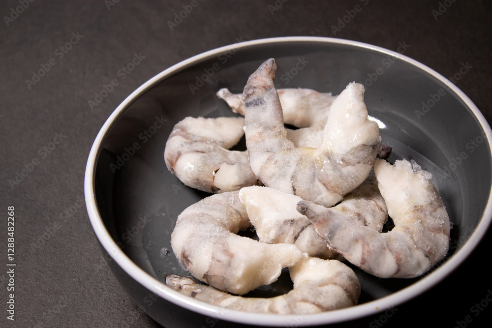 Frozen raw tiger prawns shrimps in a grey bowl on grey kitchen table Frozen raw tiger prawns shrimps in a grey bowl on grey kitchen table