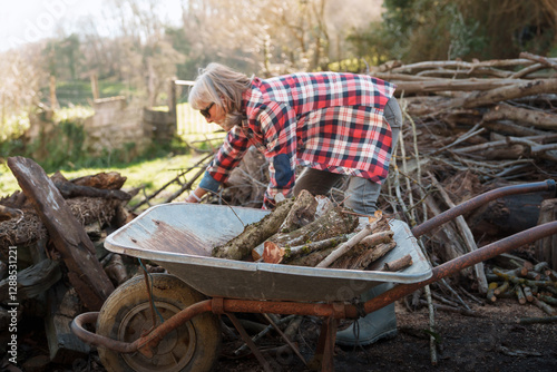 Woman farmer loading firewood into wheelbarrow in countryside