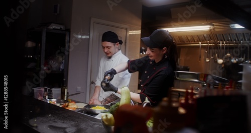 Tableau sur toile A man and a woman in a chef's uniform talk and smile while cooking in the restau