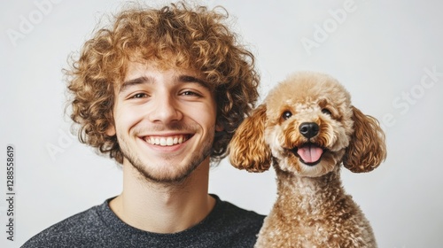 Handsome man with dark curly hair looking at camera and smiling, nearby funny red poodle looking at camera, white plain background