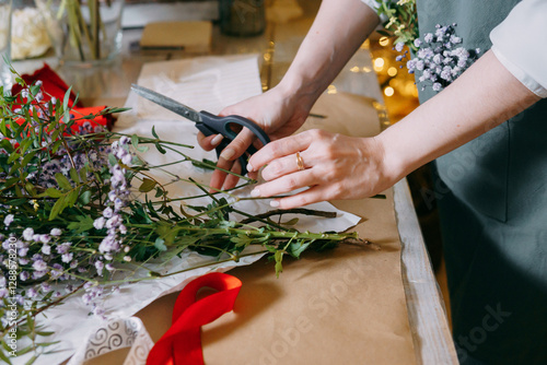 A florist works on preparing beautiful floral arrangement. Various flowers and materials lie on table, emphasizing the artistic and inspiring atmosphere associated with floral design and presentation.
