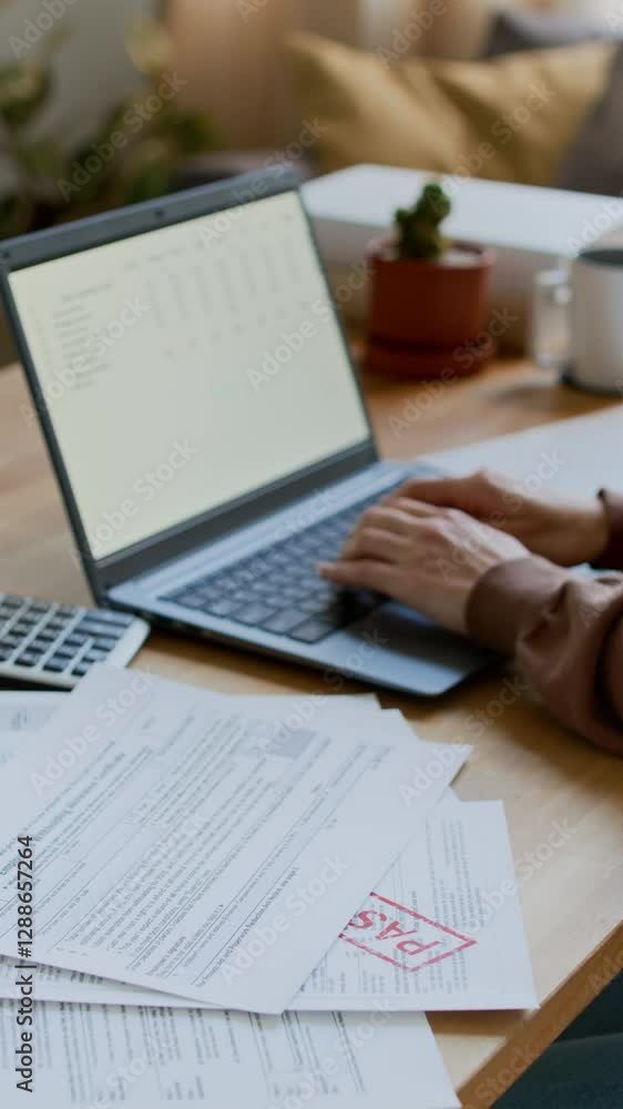 Vertical closeup of hands of unrecognizable female homeowner sitting at desk at home, sorting through unpaid utility bills and overdue invoices, then typing on laptop while managing personal budget