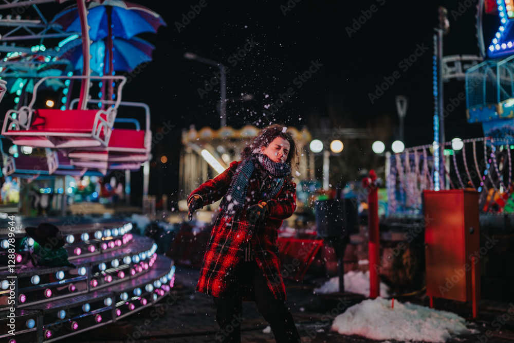 Obraz premium A woman enjoying herself on a snowy night at a brightly lit amusement park. The scene captures her playful and joyful mood alongside the festive colors of the winter season.