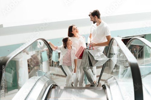 Family, father, mother and daughter are going up on escalator in shopping mall.