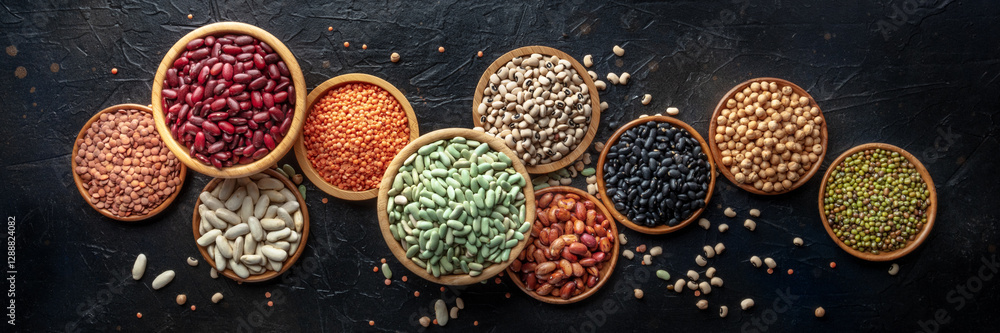 Obraz premium Various legumes, overhead flat lay panorama on a black background. Many different pulses, an assortment, panoramic banner