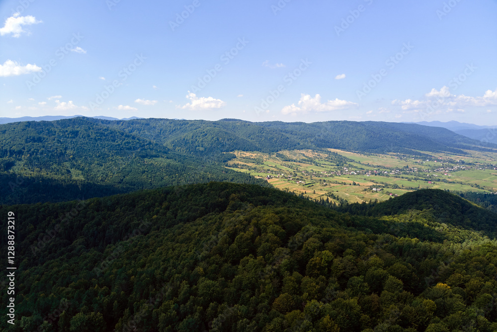 Fototapeta premium Aerial view of mountain hills covered with dense green lush woods on bright summer day