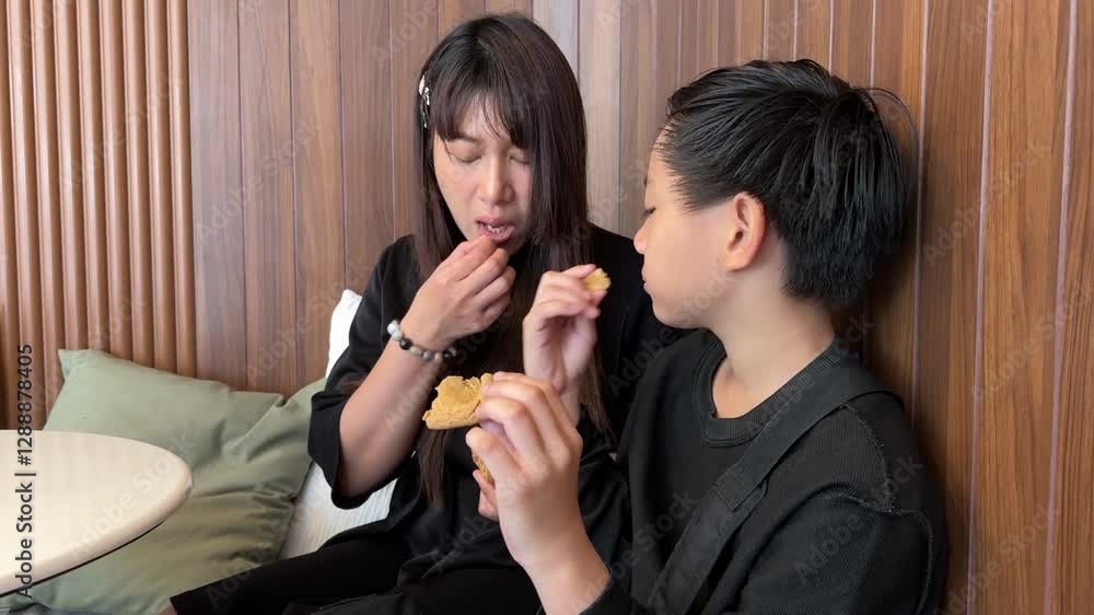 A Southeast Asian single mom eating a snack with her son in a coffee shop during the day.