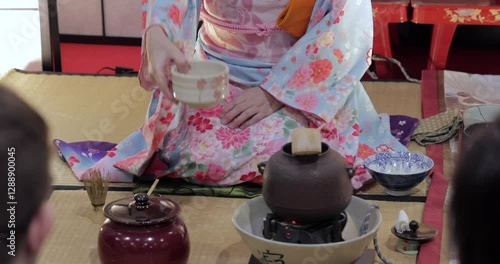 Tea master in a kimono carefully handing a ceramic tea bowl during a Japanese tea ceremony, showing the correct way to receive and hold it