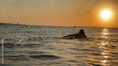Long-haired man surfer lying and paddling on a surfboard in the Indian Ocean at sunset time. Waiting for his wave.
