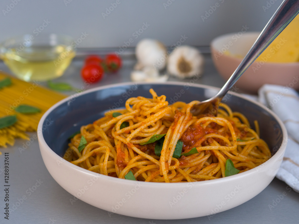 Lifting balanesi pasta twirled with tomato sauce, garnished with fresh basil, resting in contemporary dishware near softly blurred spaghetti and cherry tomatoes