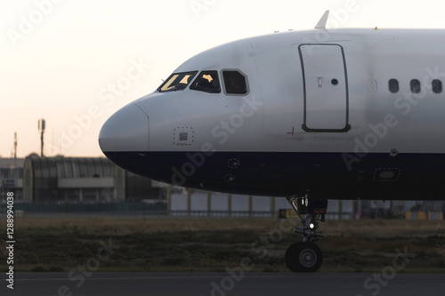 Commercial jet rolling along tarmac, sunset glowing behind sleek aircraft, highlighting runway before takeoff