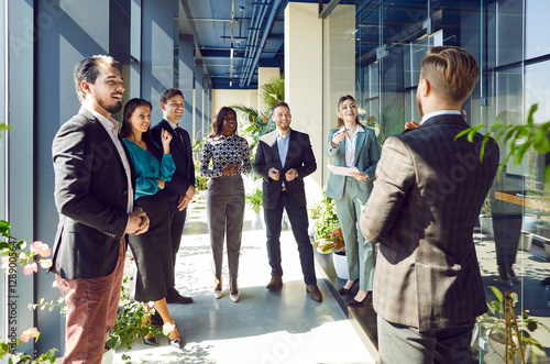 Boss and group of happy business people standing in lobby of modern office. Multicultural team smiling looking at business man. Concept business success, employee appreciation day, common group photo