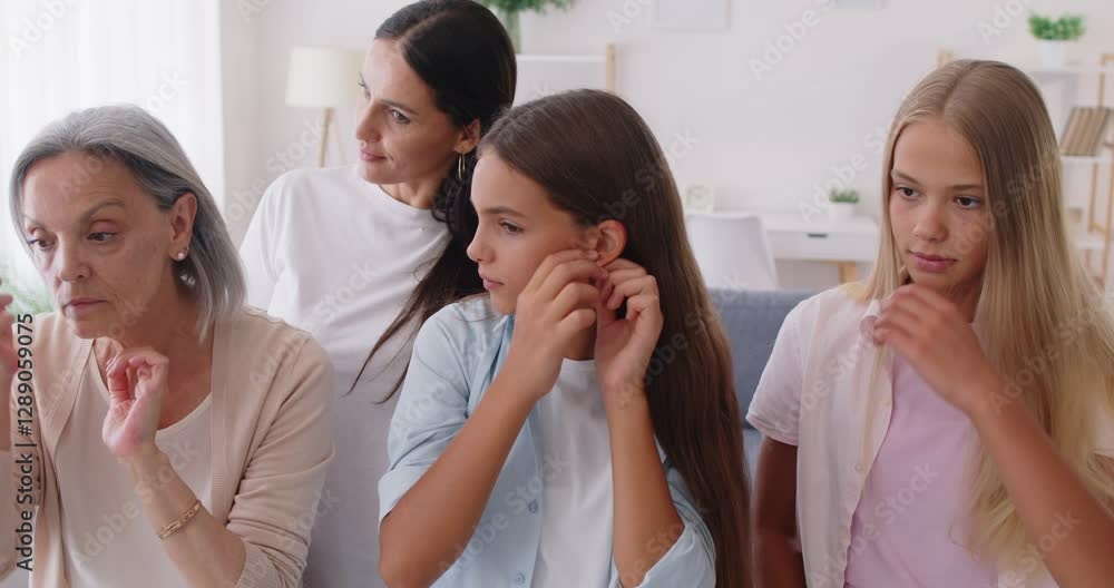 Four women from different generations gather in front of mirror, engaging in personal grooming. Teenage girls, together with their mother and grandmother, comb hair, put on earrings and mend clothes. Four women from different generations gather in front of mirror, engaging in personal grooming. Teenage girls, together with their mother and grandmother, comb hair, put on earrings and mend clothes.