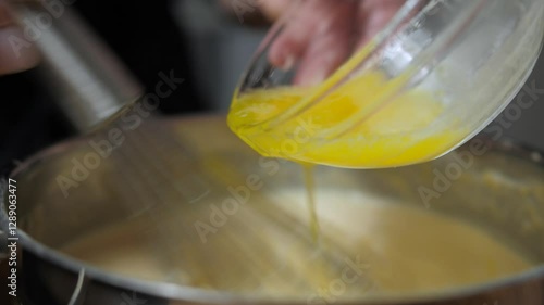 Preparation of pancake batter. The cook mixes a mixture of eggs, sugar and milk in a dark bowl, adding melted butter. Kneading the dough with a metal mixer.