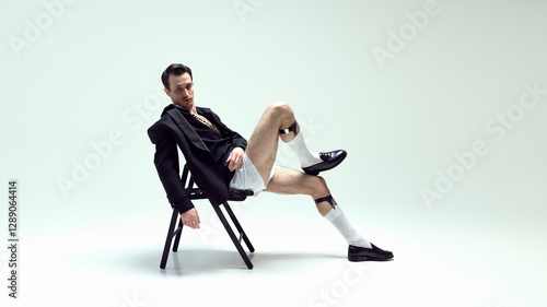 Fotografie Stylish young man model reclining on chair with nonchalant attitude and relaxed pose against white studio background