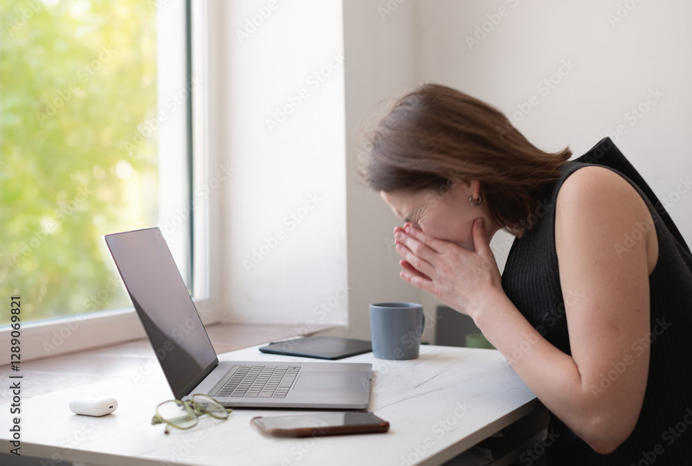 Woman working remotely from home, sitting at desk with laptop, sneezing due to illness during overtime. Woman working remotely from home, sitting at desk with laptop, sneezing due to illness during overtime.